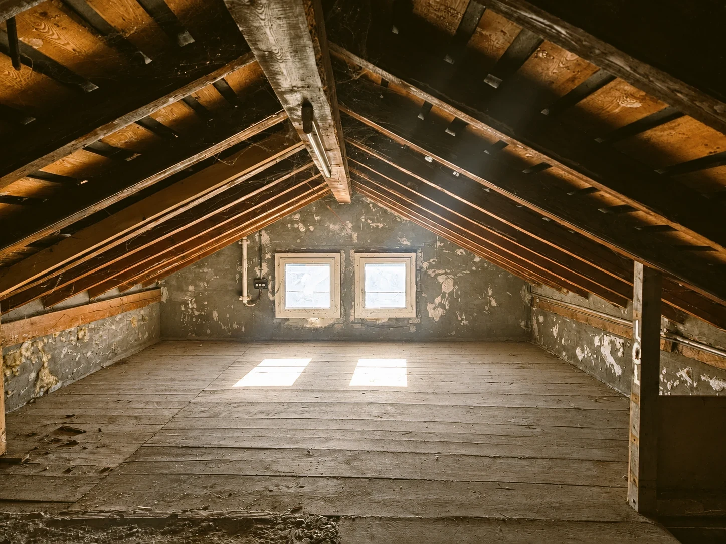 Un comble vide sous les chevrons, plancher de planches et murs à l’enduit écaillé ; au fond, deux petites fenêtres carrées dans le pignon