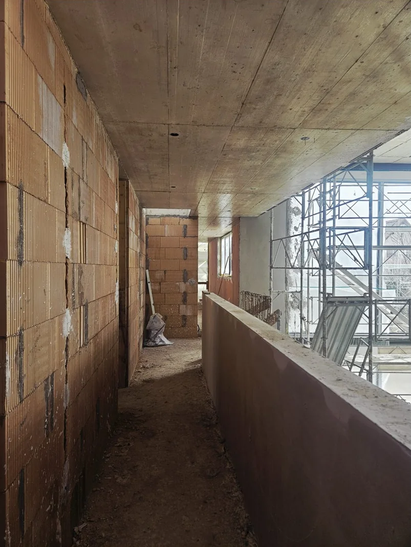 La galerie intérieure du 1er étage en chantier : un couloir entre un mur de briques et un muret, vitré sur un côté